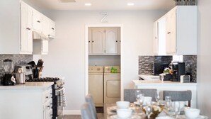 A modern kitchen with white cabinets, a stove, and a dining area set for six.
