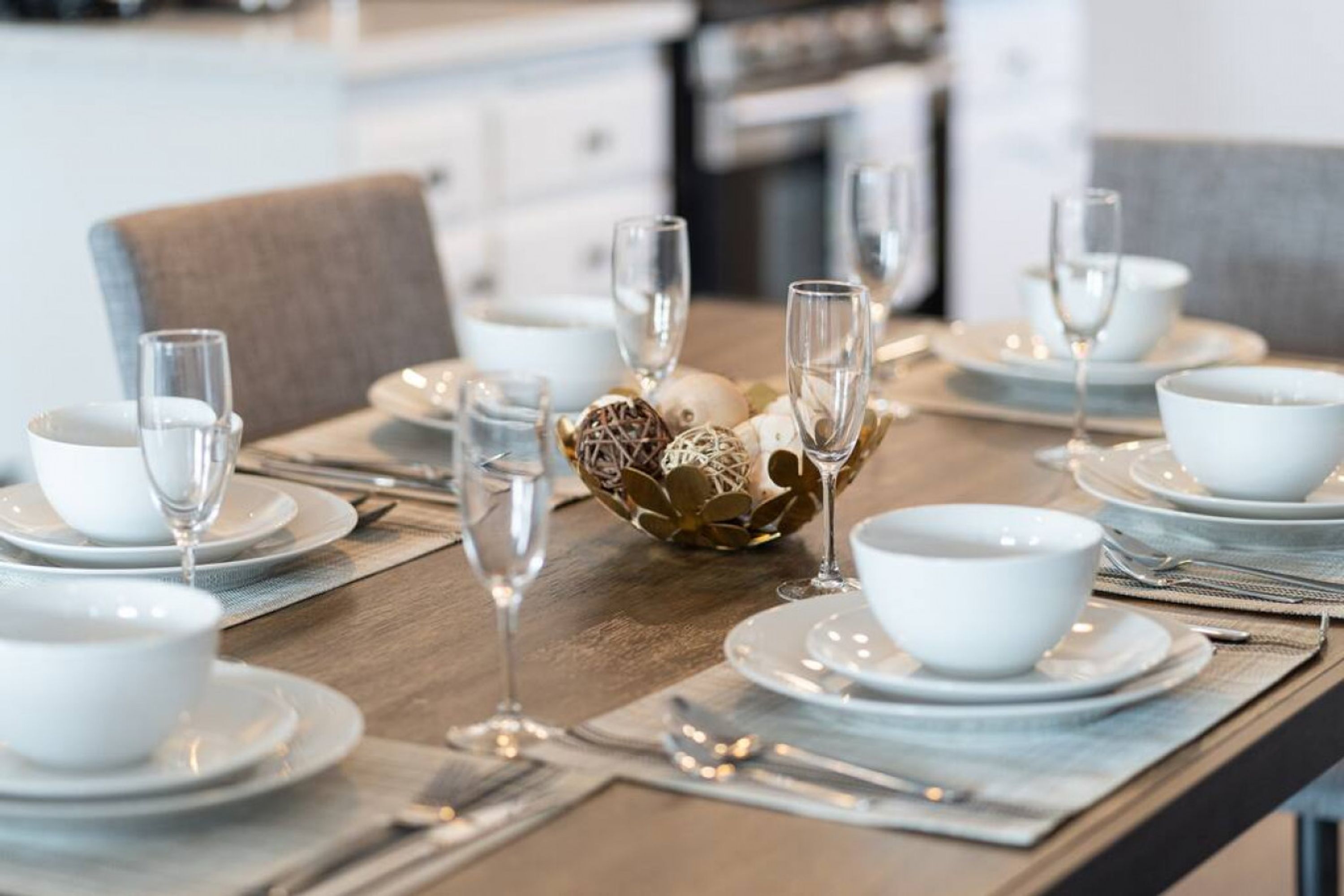 A dining table set with white plates, bowls, and glasses, with a decorative centerpiece.