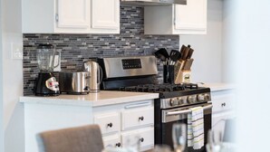 A modern kitchen with a black and stainless steel stove, a coffee maker, and a blender. There are white cabinets and a tiled backsplash.