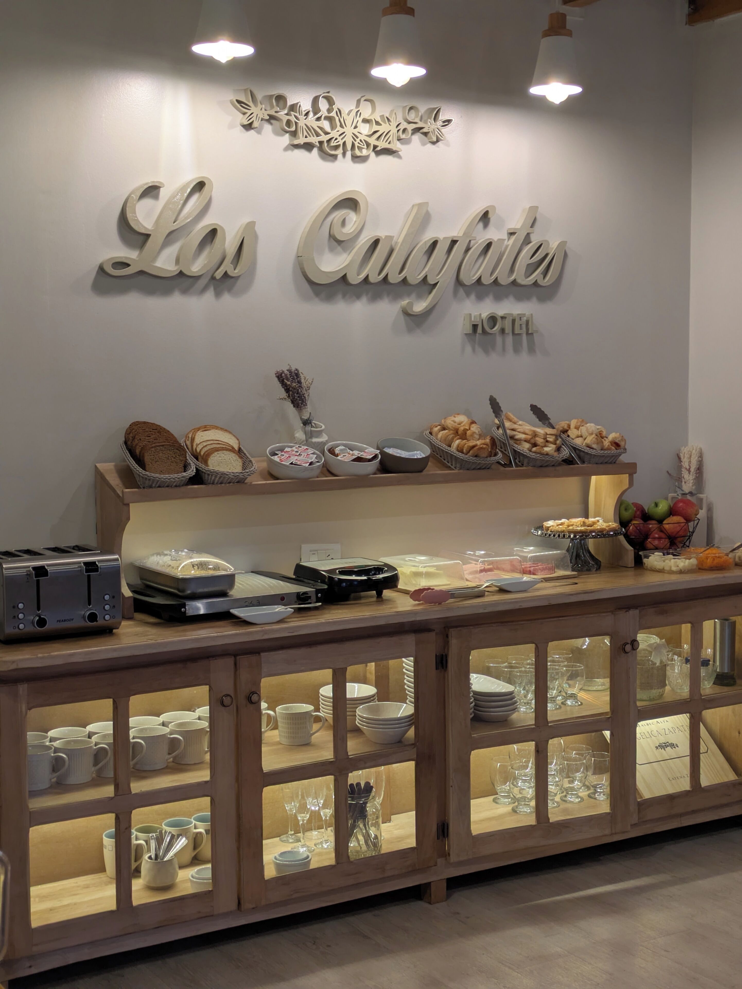 A hotel buffet area with a sign reading 'Los Calefates HOTEL' and various food items displayed.