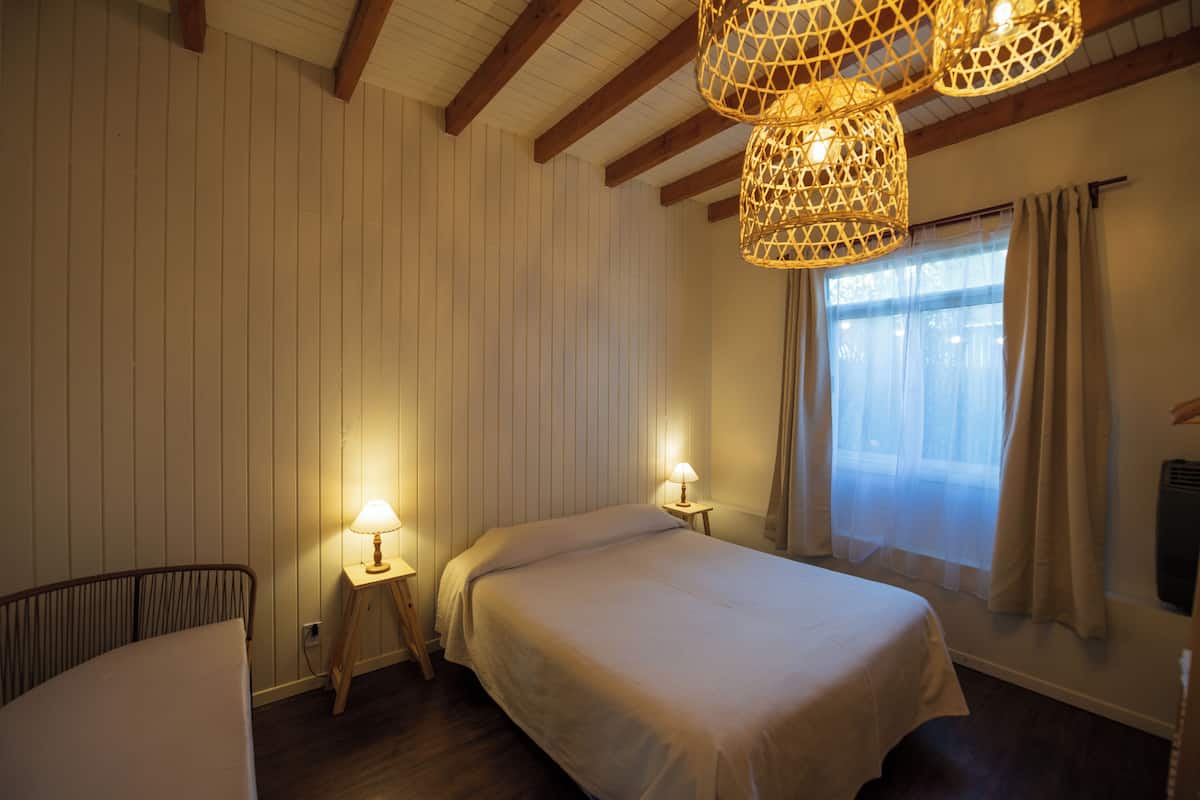 Een slaapkamer met twee bedden, houten balken, een raam met gordijnen en twee wandlampen.