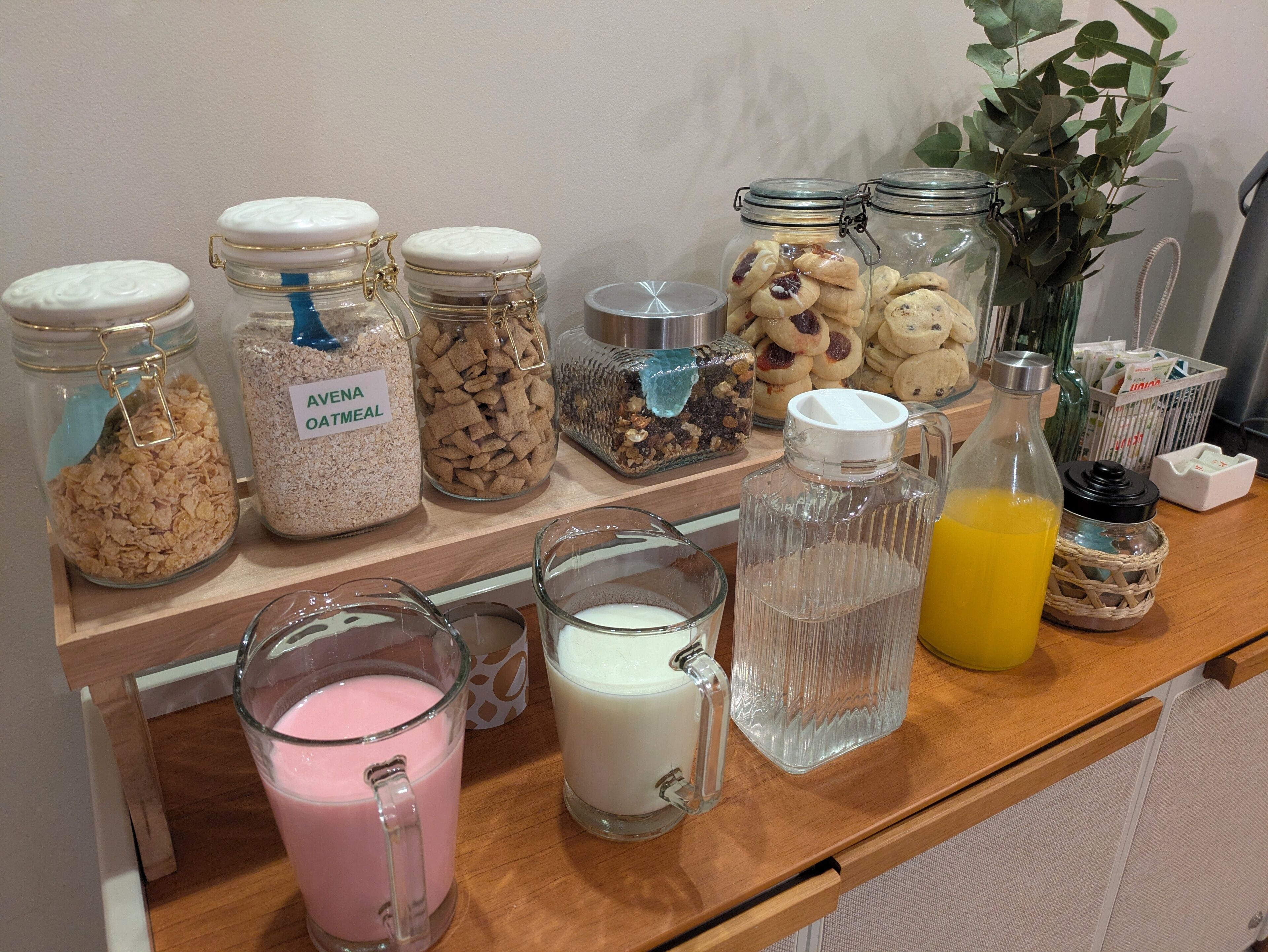 Ein Regal mit verschiedenen Lebensmitteln und Getränken, darunter Gläser mit Haferflocken, Müsli und Keksen, sowie Milch- und Saftflaschen.