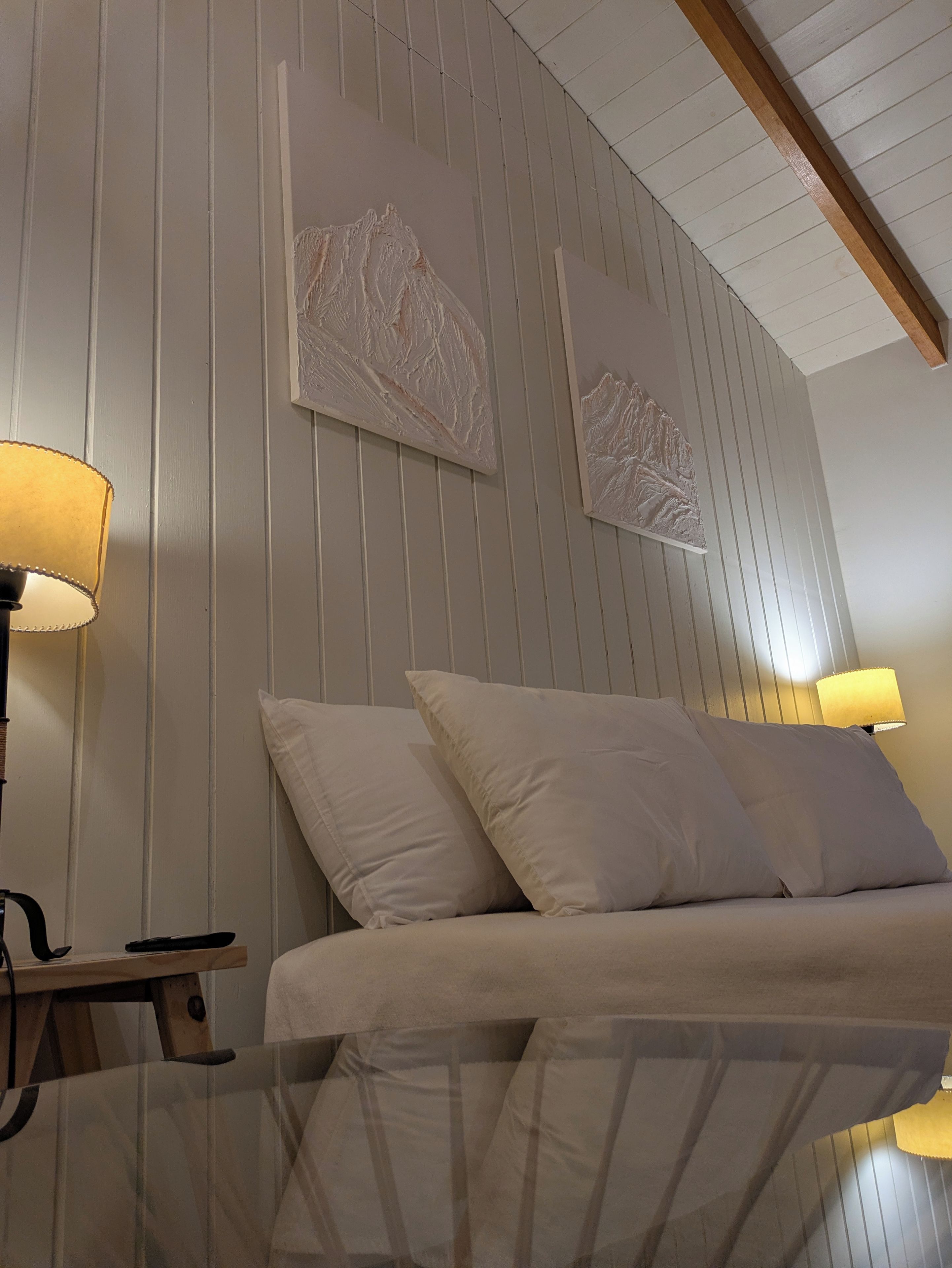 Een kamer met een bed, twee wandlampen en twee kunstwerken aan de muur.