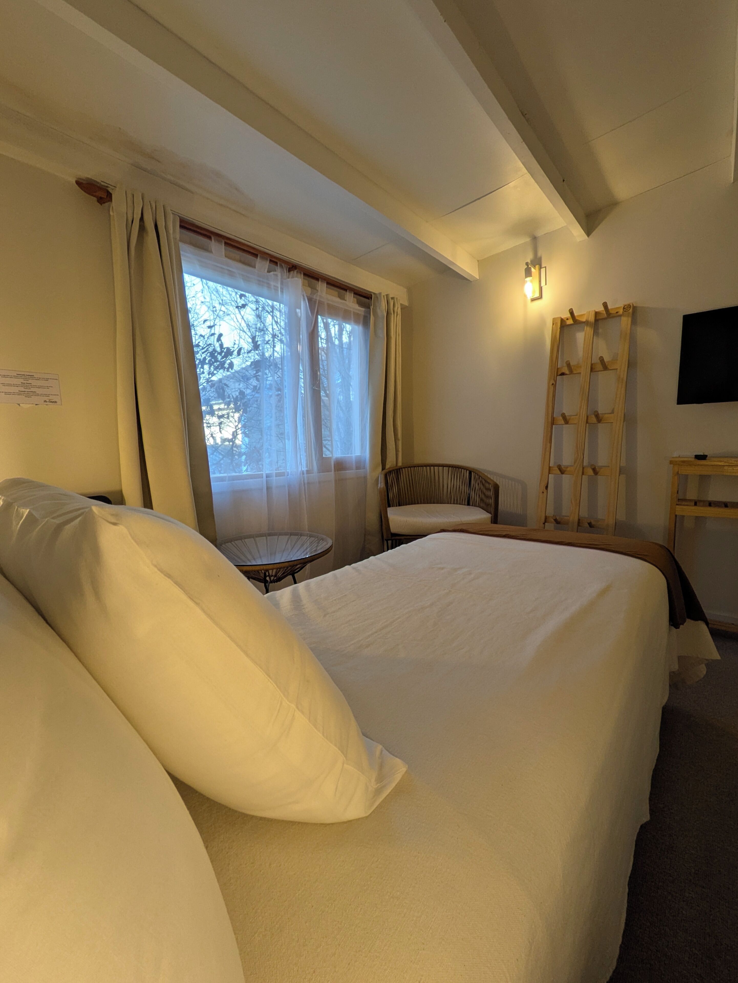 Une chambre d’hôtel avec un grand lit, une chaise, une petite table, une échelle et un téléviseur fixé au mur.