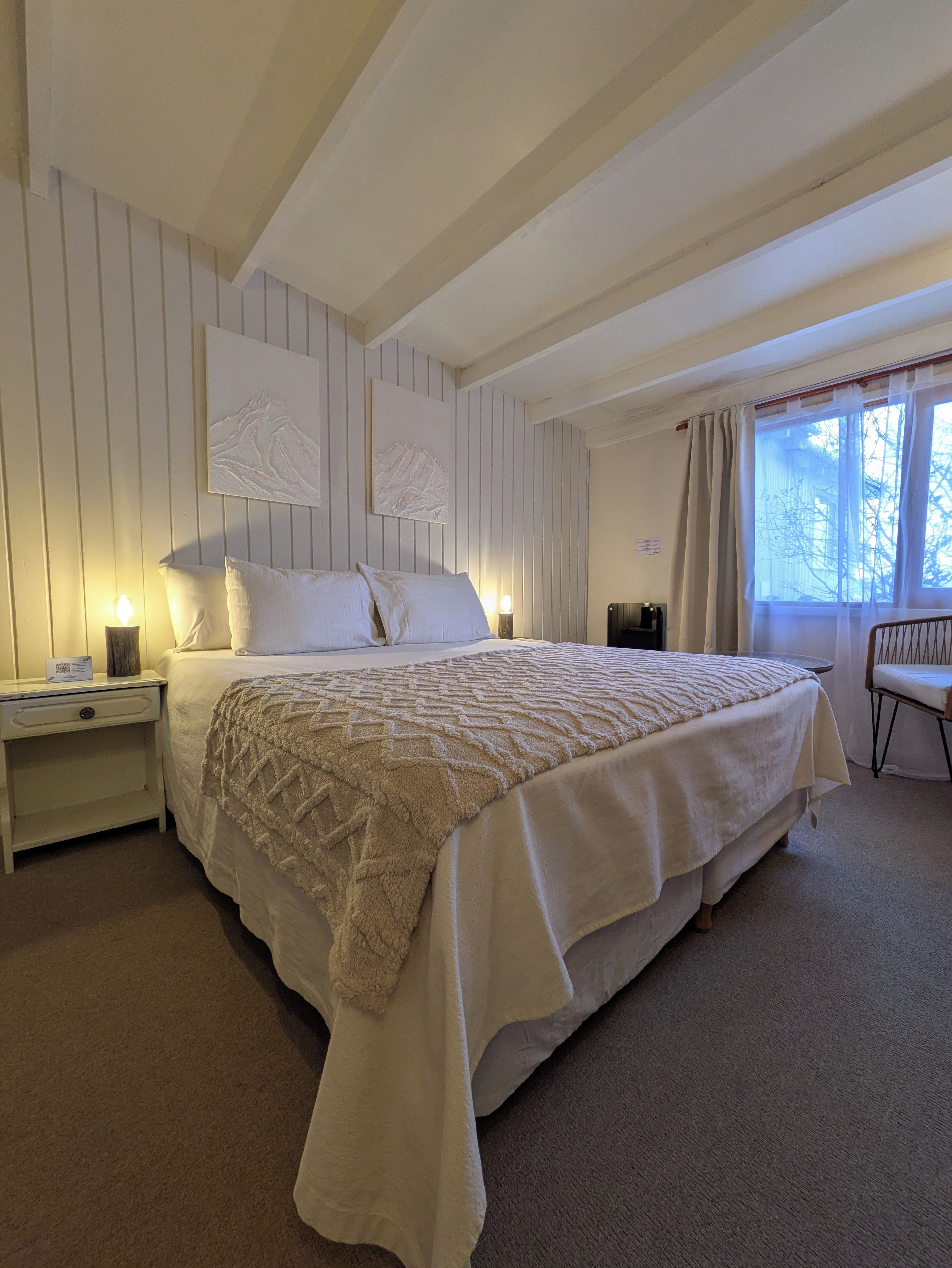 A bedroom with a large bed, two bedside tables, a chair, and a window with curtains.