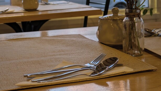 Een eettafel met een placemat, bestek, een vaas met gedroogde bloemen en een theepot.