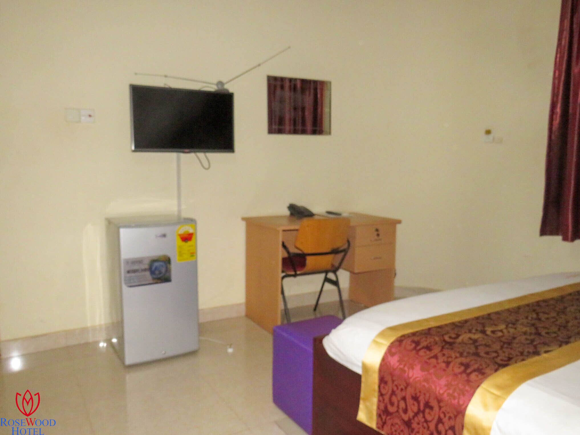 Habitación de hotel con cama, escritorio con silla, televisor montado en la pared y refrigerador.