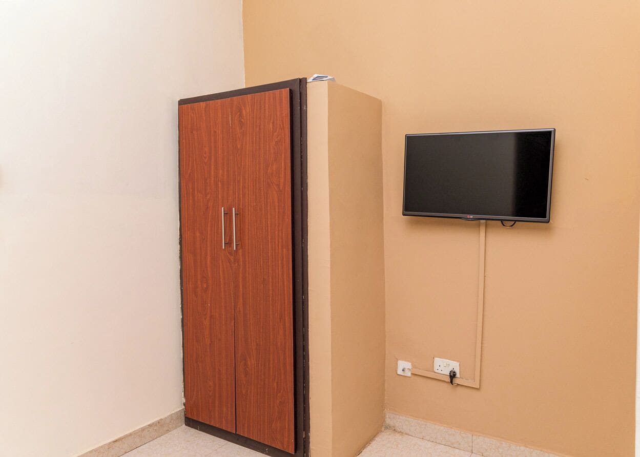 A room with a wooden wardrobe, a flat-screen TV mounted on the wall, and a power outlet.