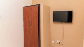 A room with a wooden wardrobe, a flat-screen TV mounted on the wall, and a power outlet.