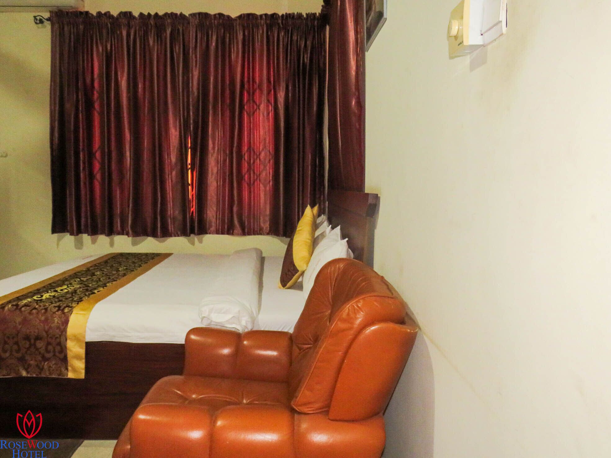 Una camera d'albergo con un letto, una poltrona in pelle marrone e una tenda.