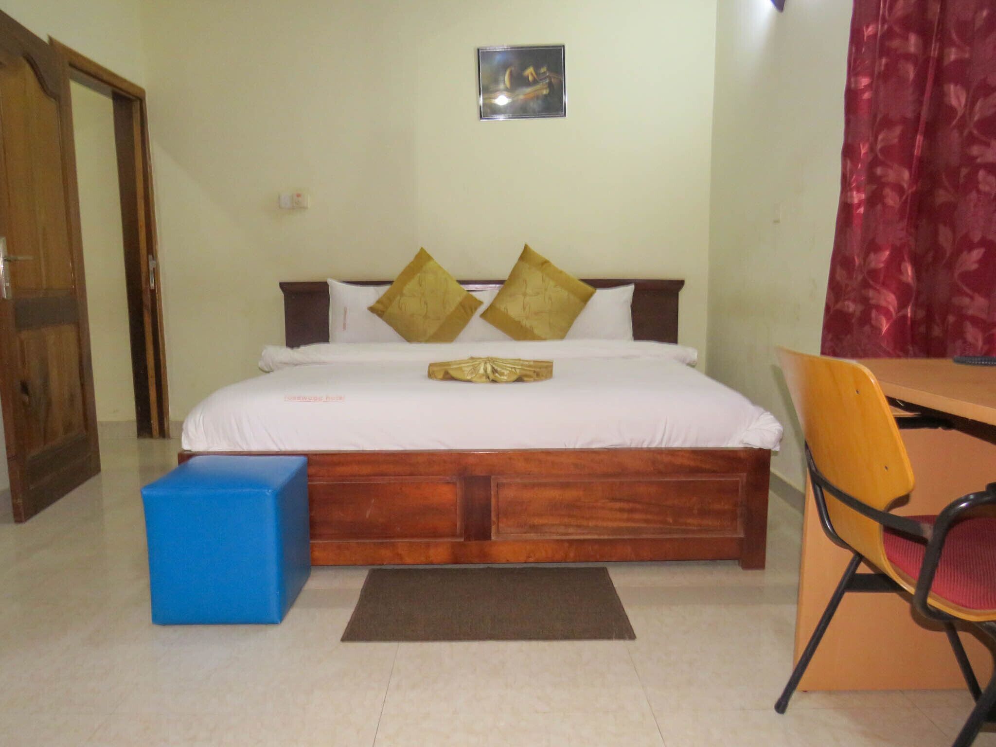 Un dormitorio con una cama de madera, dos almohadas, una mesita de noche azul, una silla y una alfombra pequeña.
