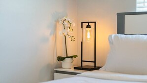A neatly made bed with white bedding, a bedside table with a potted orchid, and a floor lamp with a black frame and clear shade. - Disneyland 5BR Fullerton House Fully Remodeled 2023 w Garage Fenced Yard p61 (Fullerton)
