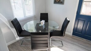 A round glass table with four black leather chairs, a blue door, and a window with blinds. - Disneyland 5BR Fullerton House Fully Remodeled 2023 w Garage Fenced Yard p61 (Fullerton)
