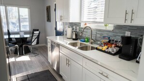 A modern kitchen with white cabinets, stainless steel appliances, and a dining area with a glass table and chairs. - Disneyland 5BR Fullerton House Fully Remodeled 2023 w Garage Fenced Yard p61 (Fullerton)