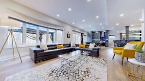 A spacious living area with a sectional sofa, a glass coffee table, and a yellow armchair. - Family Modern Walkout Basement w Sauna Ski Resort 30min (Innisfil)