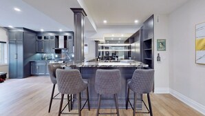 A modern kitchen with a central island, bar stools, and built-in cabinets. - Family Modern Walkout Basement w Sauna Ski Resort 30min (Innisfil)