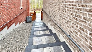 A narrow outdoor corridor with a brick wall on one side and a wooden deck on the other. - Family Modern Walkout Basement w Sauna Ski Resort 30min (Innisfil)