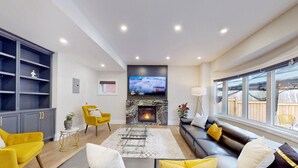 A modern living room with a fireplace, a large TV, and a view of the backyard. - Family Modern Walkout Basement w Sauna Ski Resort 30min (Innisfil)