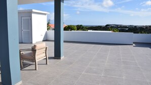 A rooftop terrace with a white door, a beige bench, and a view of the cityscape.