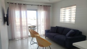 A modern living room with a dark blue sofa, a wooden chair, and a white table.