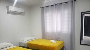 A hotel room with two beds, each with a yellow bedspread and white pillows. There is an air conditioning unit mounted on the wall above the beds.