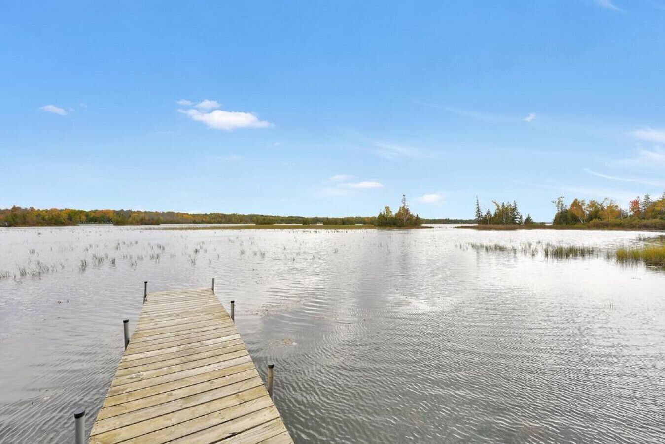 A wooden dock extending into a calm body of water with a clear sky above.