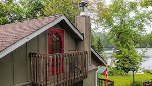 Une cabane avec une porte rouge et un balcon donnant sur un lac.