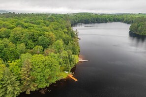 A lake surrounded by dense forest with a dock extending into the water. - Bear Essentials Lakefront Hideaway (Huntsville)