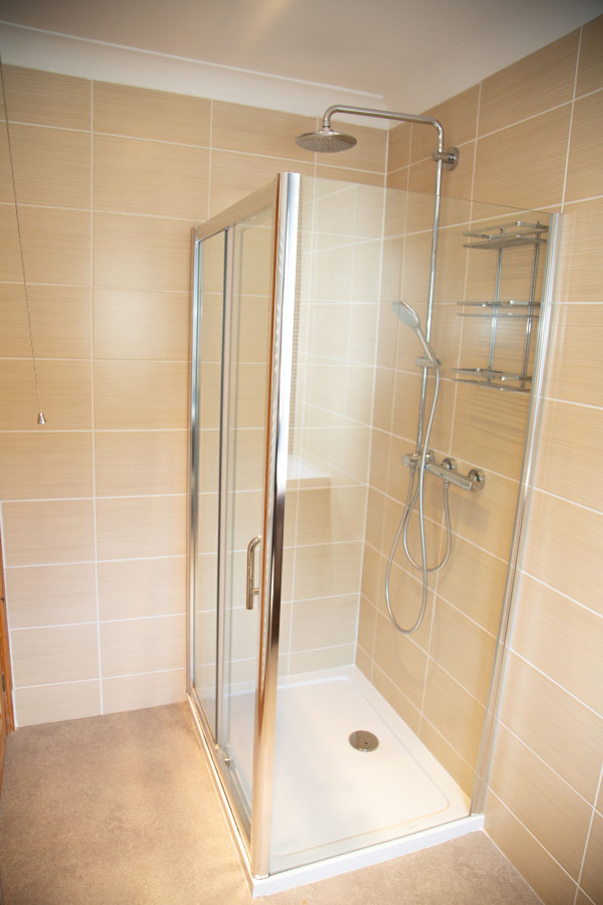 A glass-enclosed shower stall with a showerhead, a handheld showerhead, and a handheld faucet.