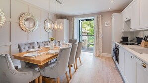 A modern dining room with a wooden table set for six, grey upholstered chairs, and pendant lighting. - Belsfield Cottage in Bowness-on-windermere (Windermere)