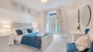 A bedroom with a large bed, bedside tables, a chair, a mirror, and a view of the outdoors. - Belsfield Cottage in Bowness-on-windermere (Windermere)