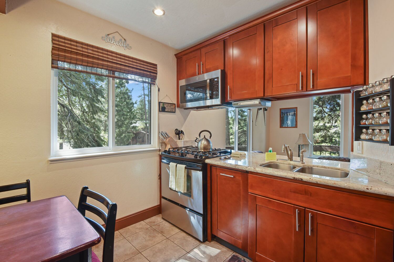 A kitchen with wooden cabinets, a stainless steel stove, a microwave, and a window with blinds.