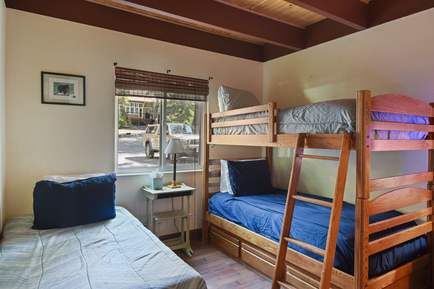 A small, cozy room with two bunk beds, a small table with a lamp, and a window with blinds.