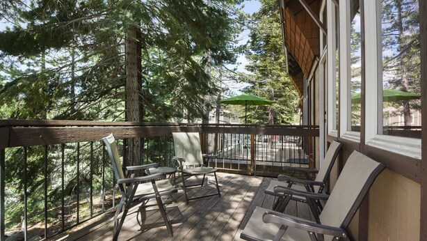 A wooden deck with four chairs and a table, surrounded by tall trees.