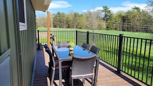 A deck with a table and chairs, a view of a green field, and a black metal fence. - Family Friendly Cottage Walking Distance to Lions Head Beach (Northern Bruce Peninsula)