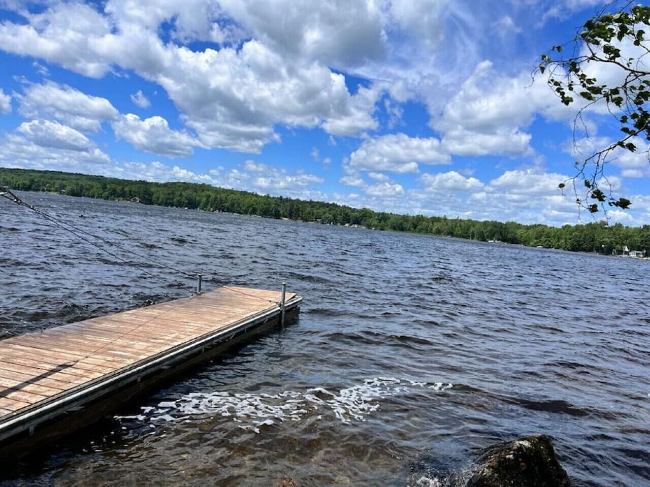 A wooden dock extending into a lake with a forested shoreline in the background.