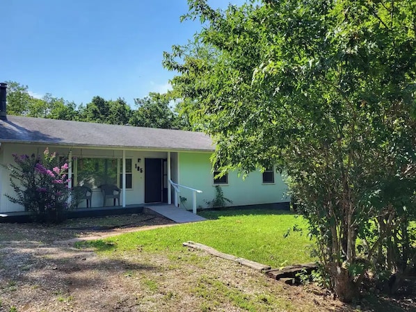 A single-story house with a front porch, a small front yard, and a tree to the right.