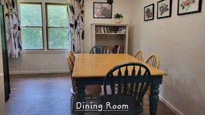 Een eetkamer met een houten tafel en stoelen, een kroonluchter en lijstwerken aan de muur.
