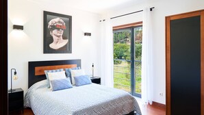 A bedroom with a large bed, a nightstand, a wall-mounted light, a framed picture, and a sliding glass door to a balcony. - Casa do Moinho - V3 w/ Private Pool (Abrantes)