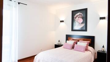 A bedroom with a bed, two bedside tables, a wall-mounted light, and a window with a curtain.
