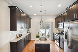 A modern kitchen with dark cabinets, stainless steel appliances, and a central island. - Zen Vibes Townhouse with Rooftop Deck Skyline View (Philadelphia)