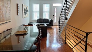 Uma sala de estar moderna com uma mesa de jantar de vidro, um sofá e uma escada com guarda-corpo de metal.