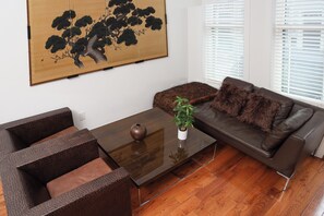 A modern living room with a brown leather sofa, a glass coffee table, and a large traditional artwork on the wall.