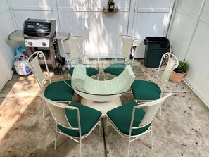A round glass table with green cushioned chairs in a covered outdoor area. - Zen Vibes Townhouse with Rooftop Deck Skyline View (Philadelphia)