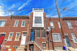 A row of red brick townhouses with white trim, a central white building, and a clear blue sky. - Zen Vibes Townhouse with Rooftop Deck Skyline View (Philadelphia)