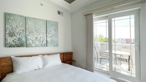 Quarto com uma cama grande, porta de correr para uma varanda e três quadros pendurados na parede.