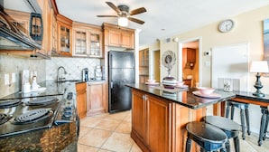 A kitchen with wooden cabinets, a black refrigerator, a stove, and a ceiling fan. - Seascape 1108 in Galveston (Galveston)