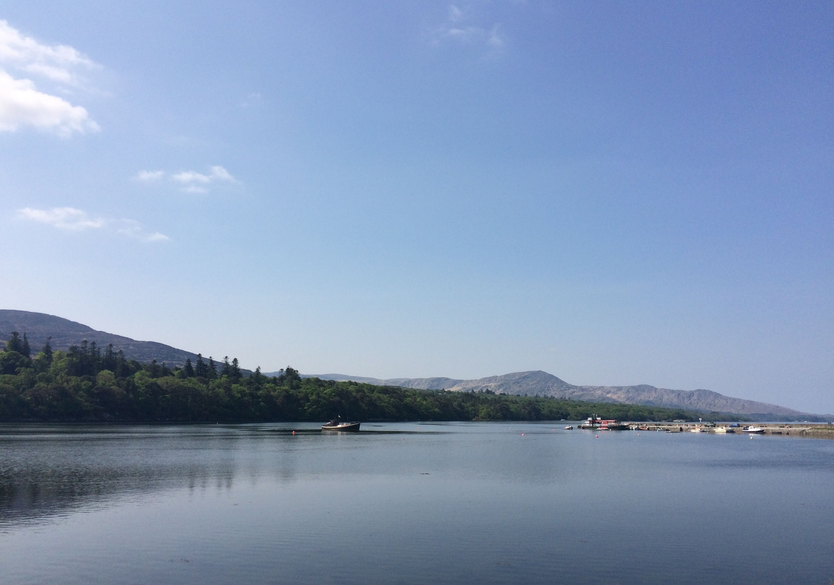 A calm lake with boats, surrounded by trees and mountains.