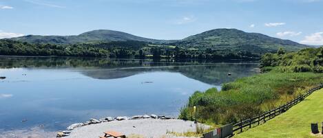 A lakeside view with a wooden fence, picnic table, and a clear sky.