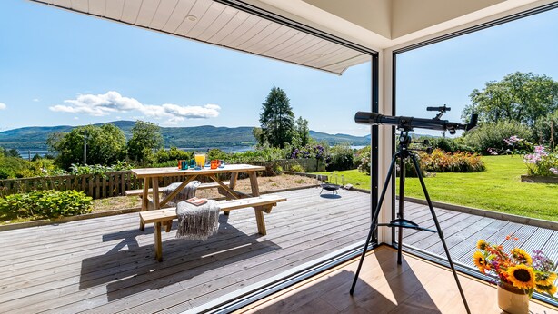 Een terras met een telescoop, een picknicktafel en uitzicht op een meer en bergen.